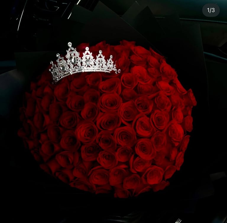 Ornate silver tiara resting on a large spherical arrangement of deep red roses against a dark background