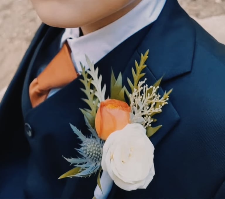 Boutonniere with white and coral roses and greenery pinned to a navy suit jacket with white collar