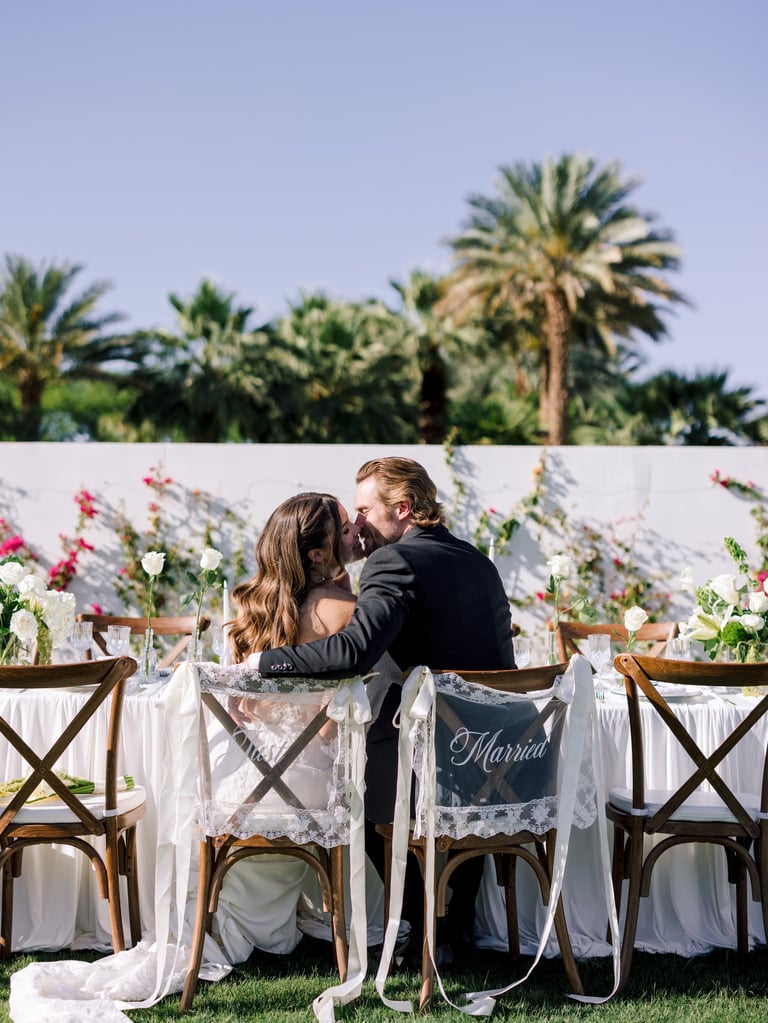 Newlyweds kissing at an outdoor wedding reception table