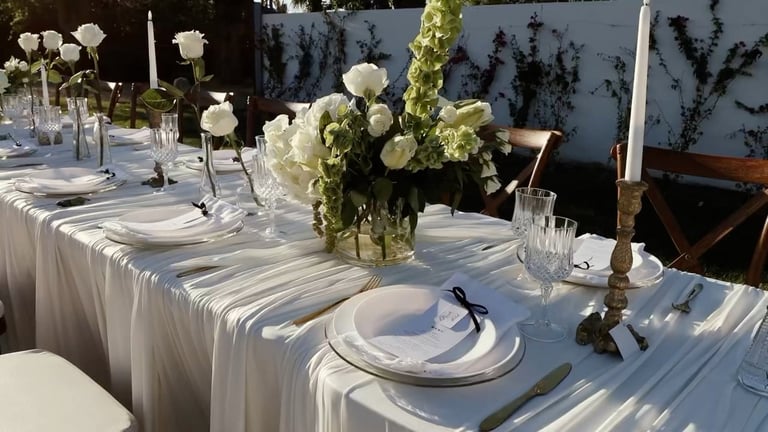 Elegant outdoor wedding reception table with white linens, place settings, and white floral centerpieces