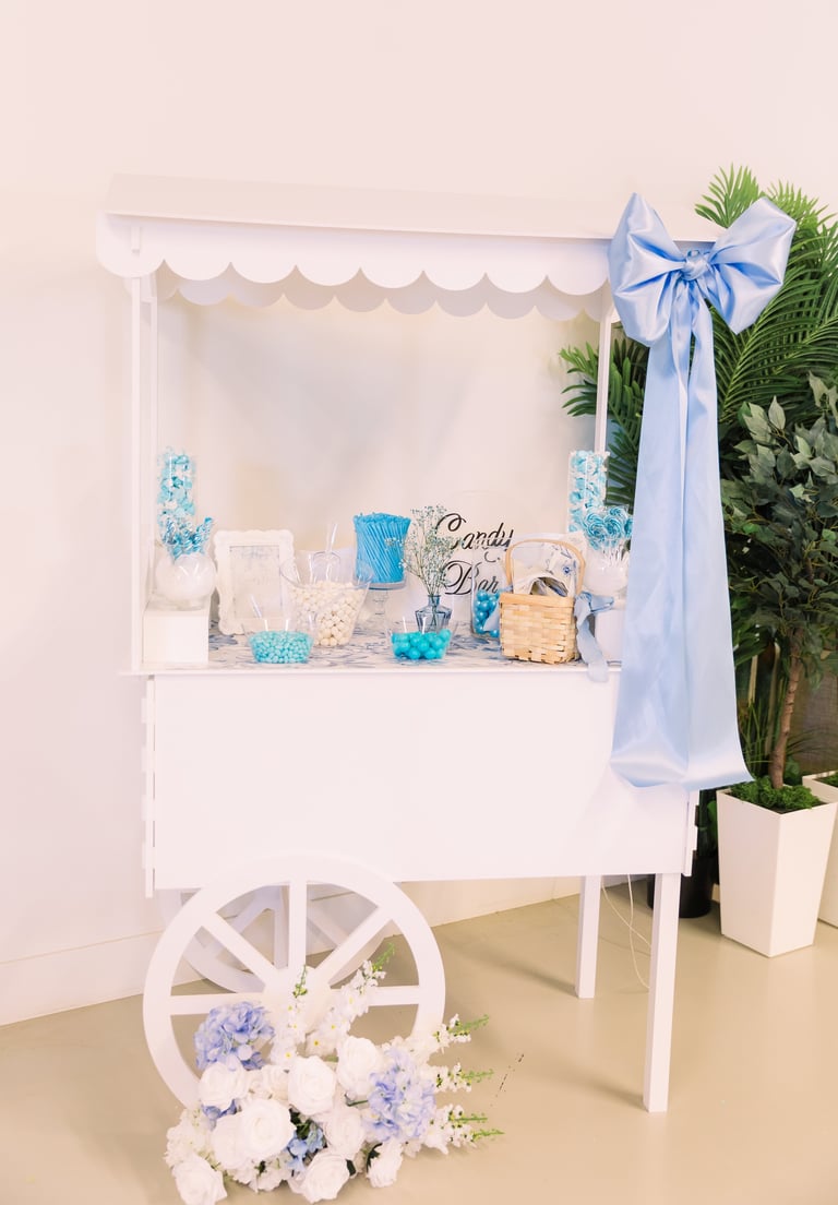 White candy cart with blue accents and flower arrangement, decorated with a blue ribbon bow