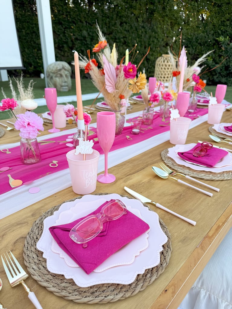 An elegant outdoor table setting featuring hot pink decorations, fresh flowers, candles, and place settings