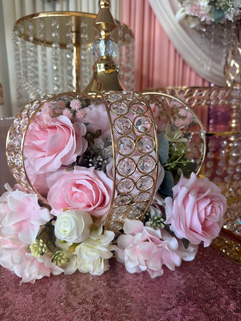 Ornate gold carriage-shaped centerpiece filled with pink and white roses and decorative flowers on a burgundy surface