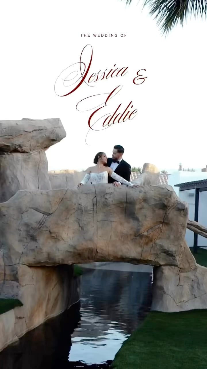 Wedding invitation cover featuring bride and groom posing on stone rocks above water with palm fronds and city skyline in background
