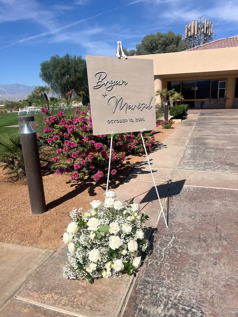 Wedding sign on easel reading Bryan and Meredith October 12 2024 with white flowers at outdoor venue entrance