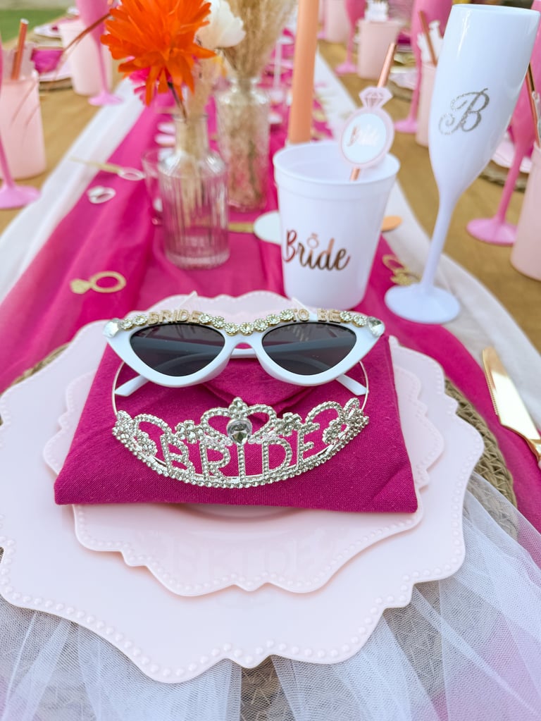 Bridal shower table setting with white heart sunglasses and BRIDE tiara on pink napkin