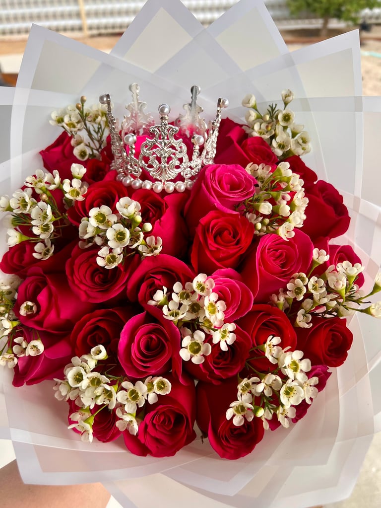 Luxurious bouquet of red roses with white babys breath flowers and a decorative tiara, wrapped in white tissue paper