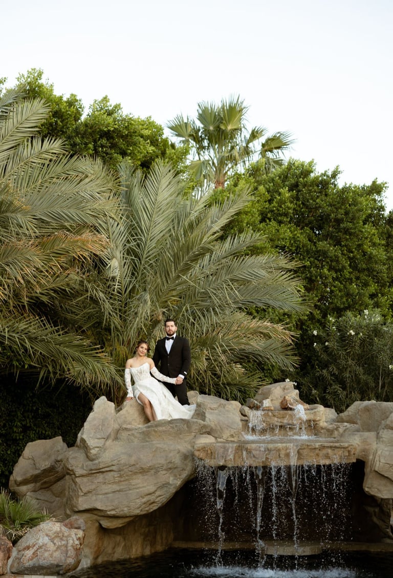 Bride and groom posing on rocks by a waterfall with lush palm trees and greenery in the background