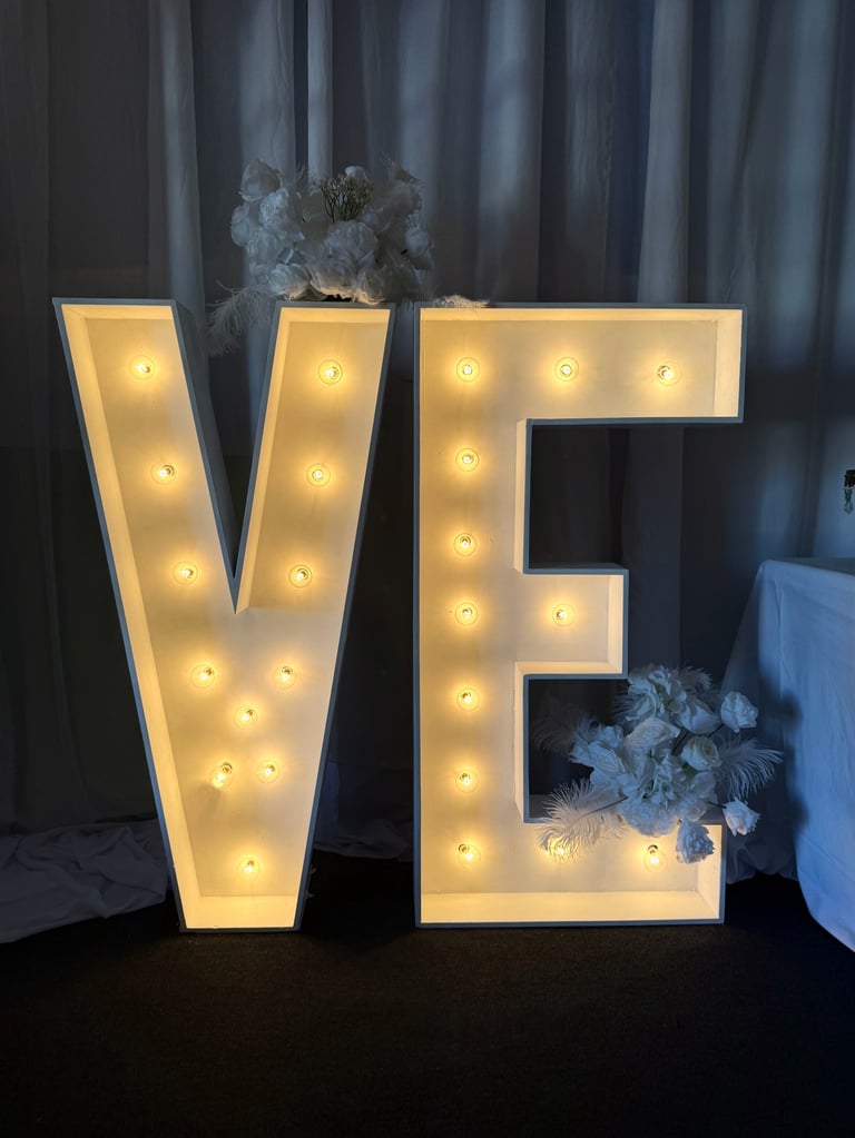 Large illuminated LOVE sign with warm white lights and blue flowers against a dark curtain backdrop