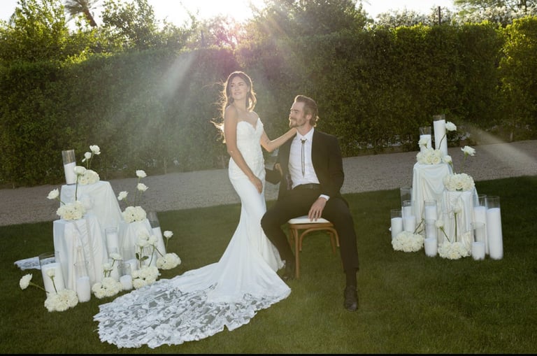Bride in white lace gown and groom in dark suit sitting on grass