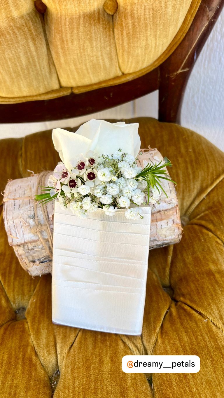 White ceramic vase with burgundy and white flowers arranged on a mustard yellow velvet chair with wooden frame