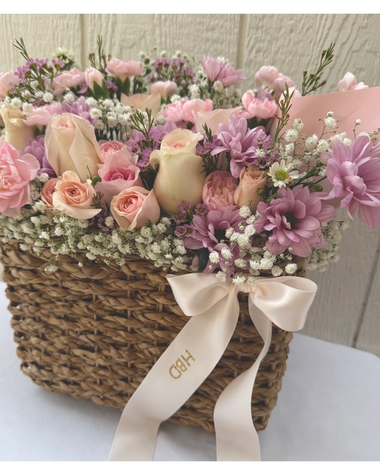 Floral arrangement in woven basket with pink roses, carnations, babys breath, and white ribbon bow