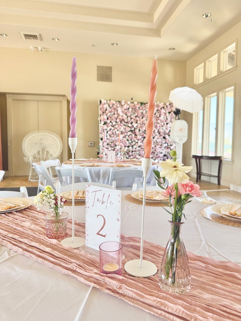Elegant wedding reception table with pink and white floral backdrop, tall twisted candles, table number 2, and flower centerpieces.