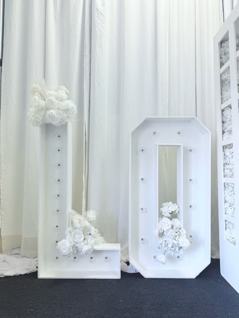 White decorative display stands with white flowers and crystal accents on dark floor against draped curtain backdrop