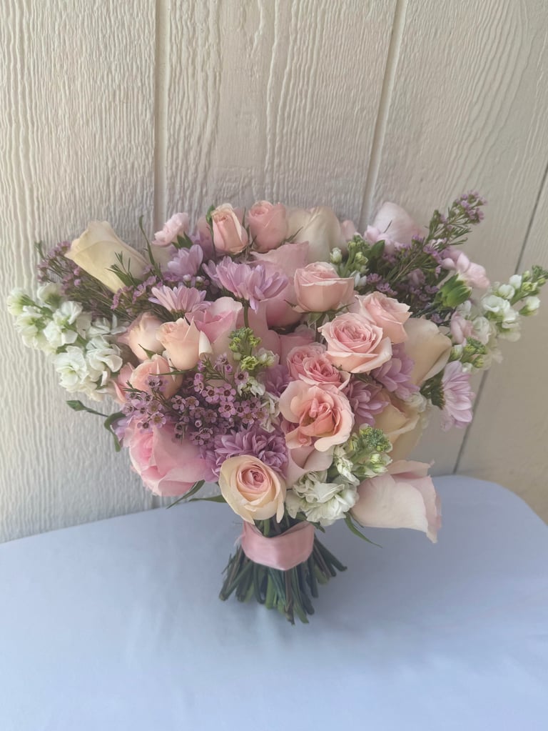 Elegant bouquet of pink roses, purple lilac, and white flowers tied with a pink ribbon, displayed on a light background