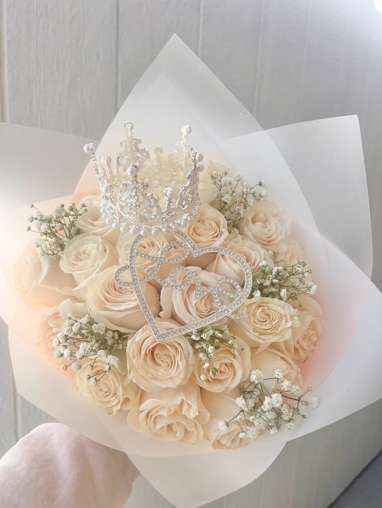 Elegant bridal bouquet of peach roses with babys breath, topped with a sparkling tiara and heart-shaped brooch, wrapped in white tissue paper