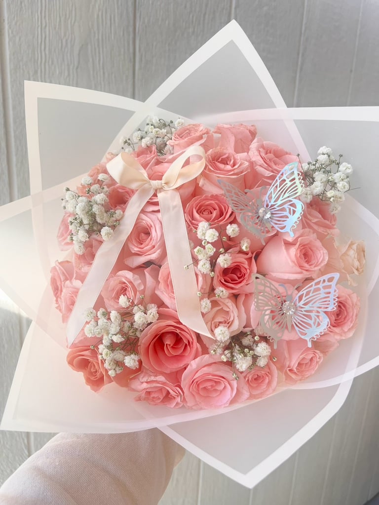Luxurious bouquet of pink roses with white babys breath flowers, white ribbon bow, and decorative butterflies on white wrapping paper