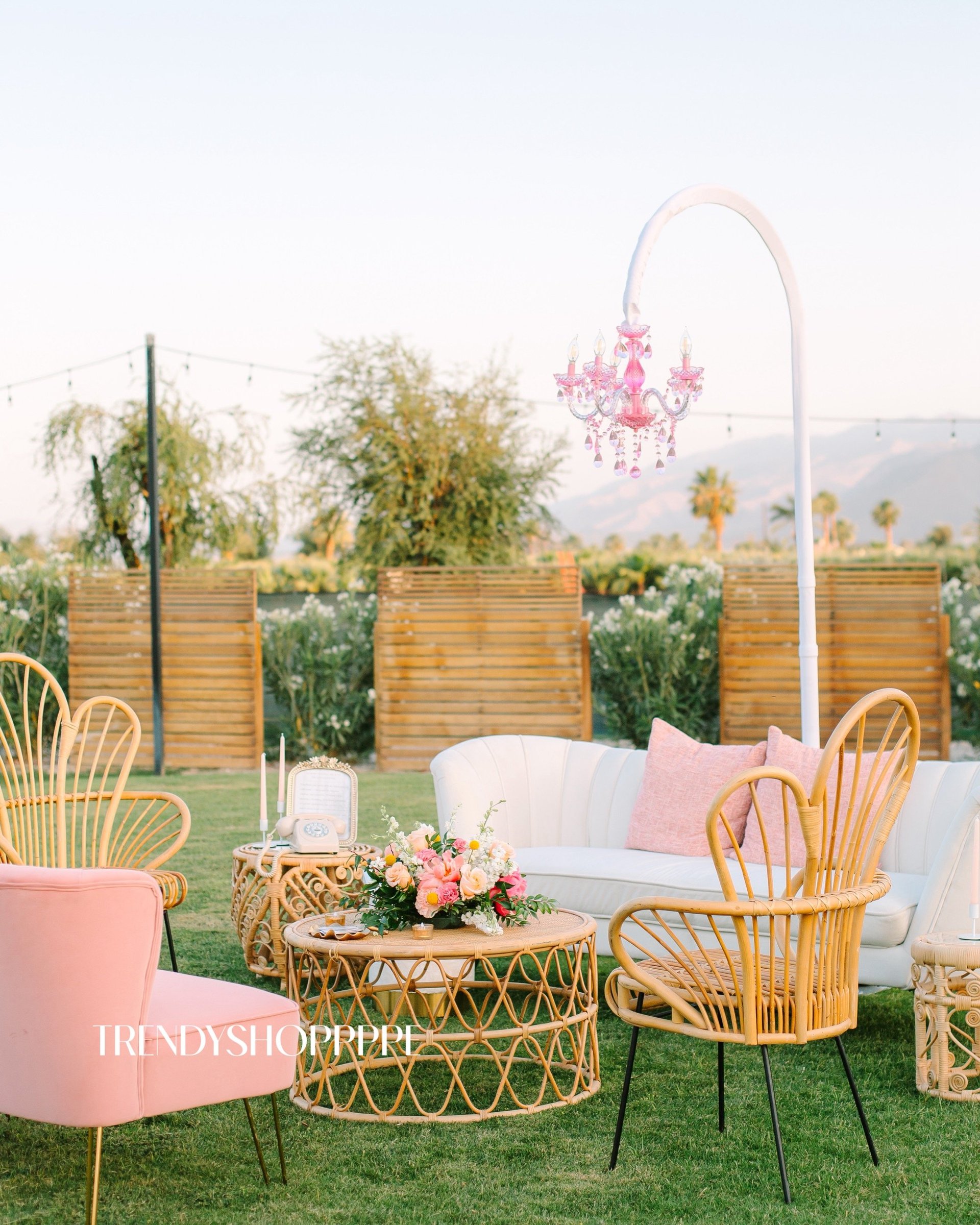 Outdoor garden seating area with pink and gold chairs, woven side table, white sofa, and pink crystal chandelier