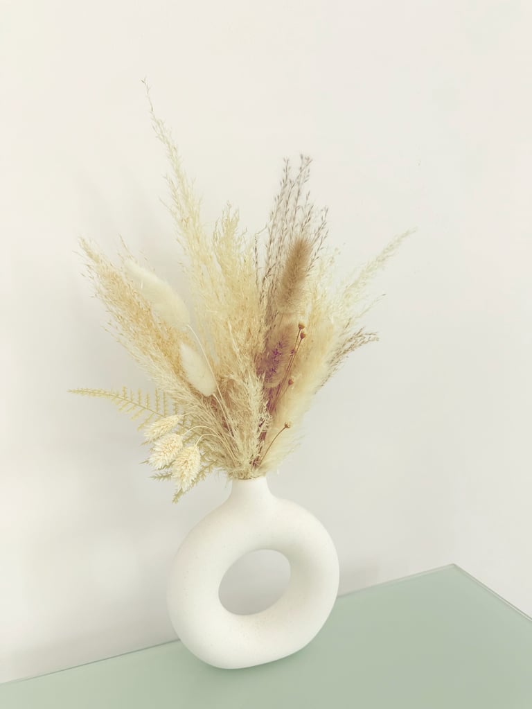 Dried pampas grass and ferns in a white ceramic vase with circular opening on mint green surface