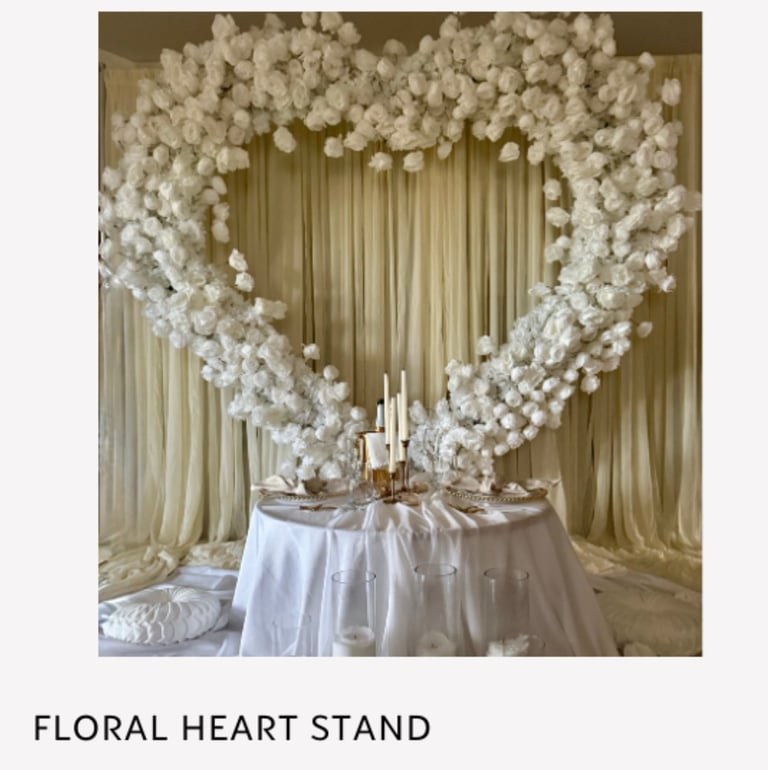 Heart-shaped floral arrangement made of white flowers hanging above a table with champagne-colored drapes and gold accents