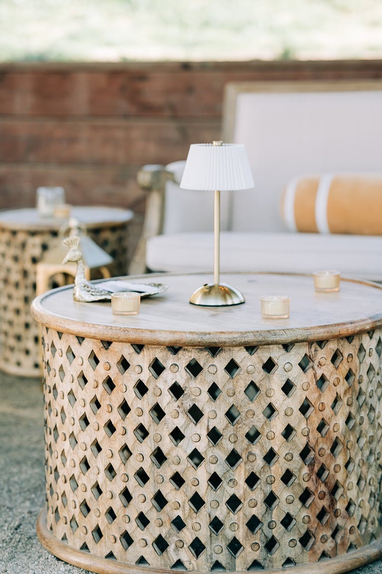 Round wooden lattice coffee table with marble top, table lamp, candles, and seating area with white sofa and patterned chair in modern living room