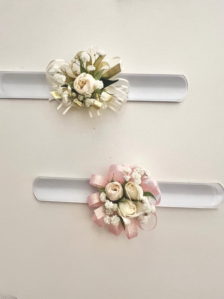 Two decorative wrist corsages with cream and pink flowers on white satin bands