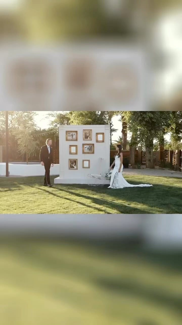 Bride and groom standing by a white panel with photo frames in a sunny garden setting