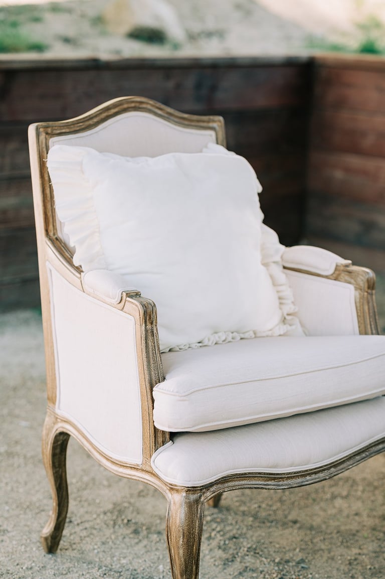 Vintage wingback armchair with white cushions and ornate wooden frame in cream and gold tones