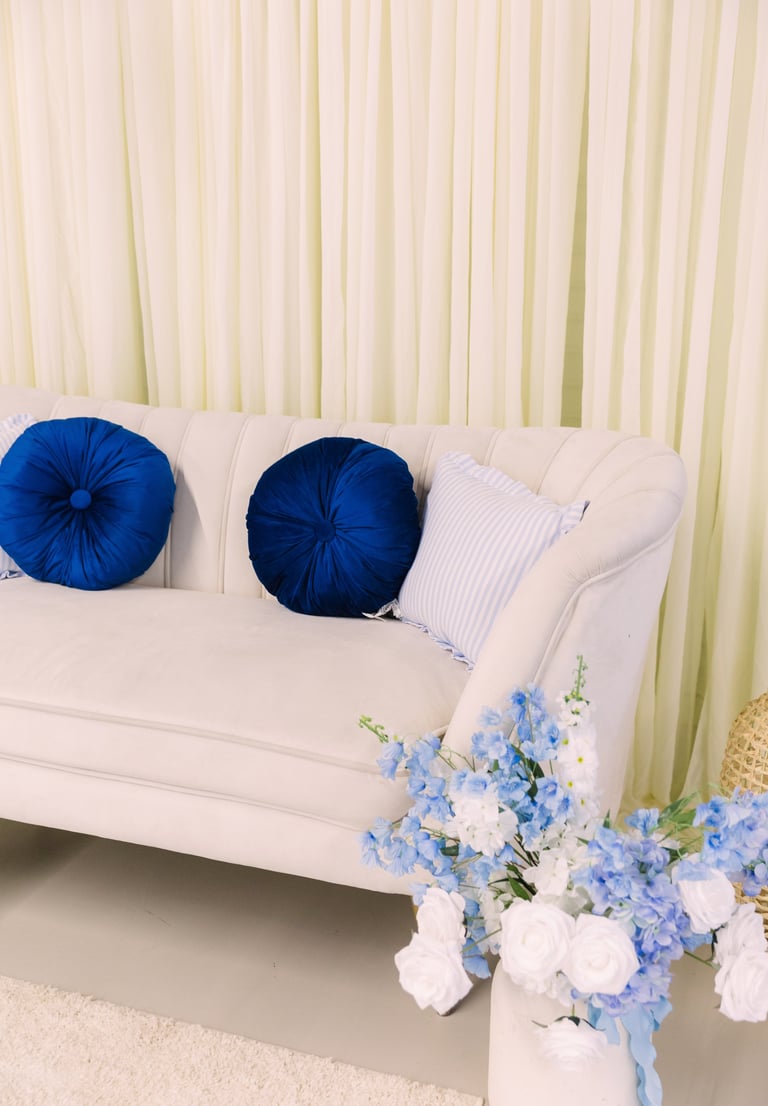 White sofa with blue velvet round pillows and striped accent pillow against cream curtains