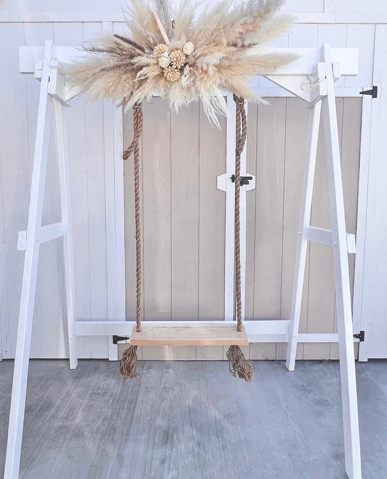 White wooden swing with rope suspended from rustic arch
