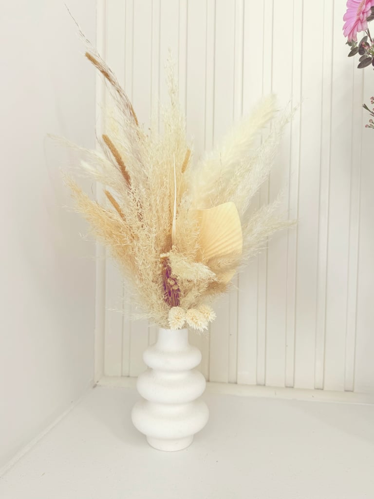 Dried pampas grass and wheat in a white ceramic vase against a white striped wall