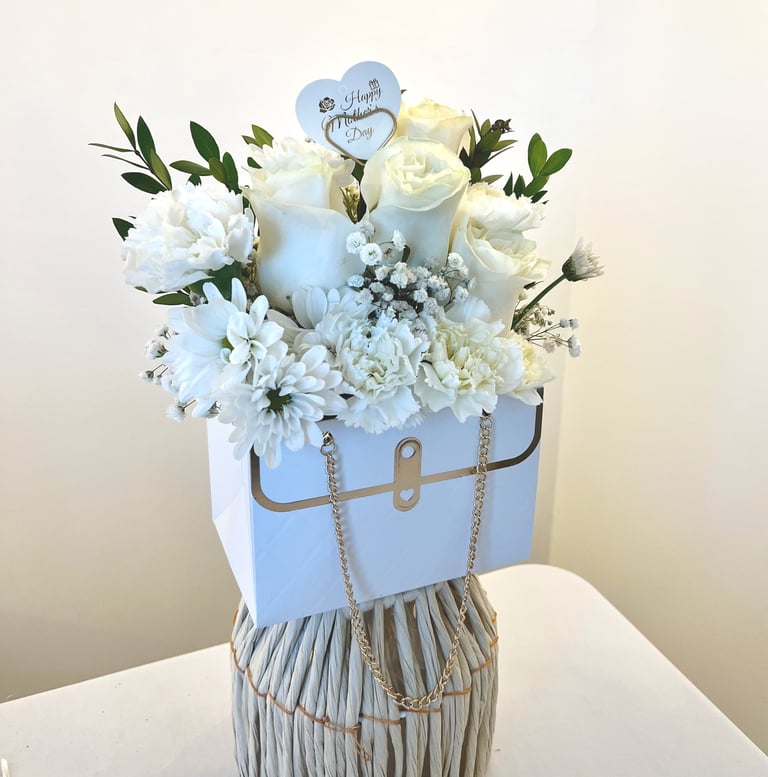 Elegant floral arrangement in light blue box with white flowers, candles, and blue heart-shaped Happy Birthday topper on white surface