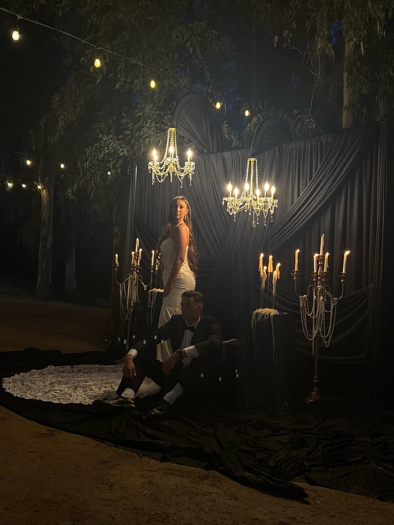 Elegant nighttime outdoor scene with man kneeling before woman in white dress, surrounded by ornate chandeliers and draped fabric under tree branches