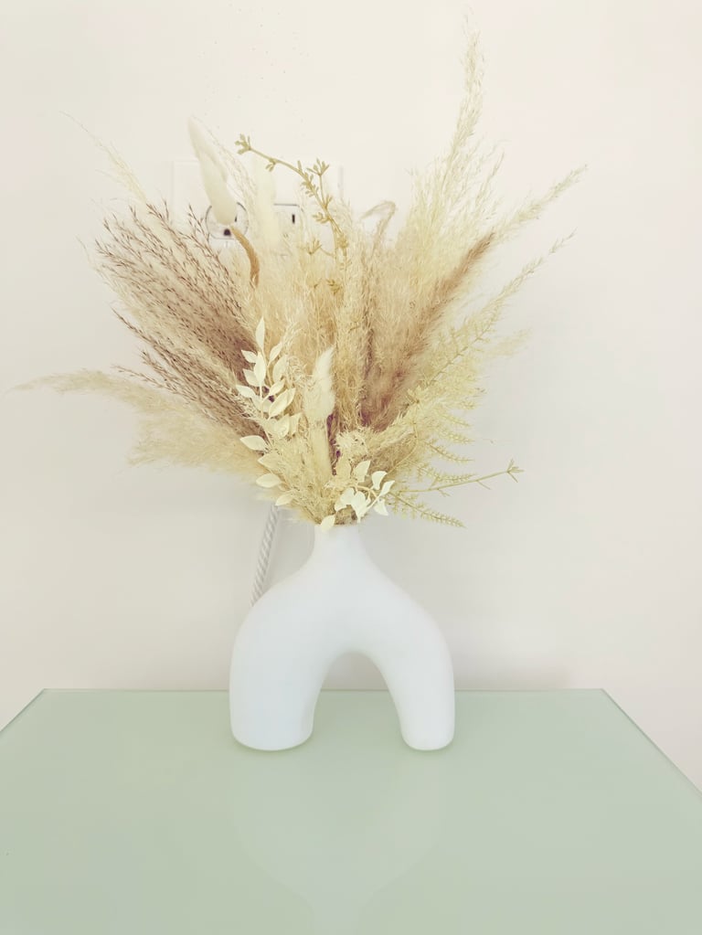 Dried pampas grass and wheat bouquet arranged in a white sculptural arch vase on a mint green surface