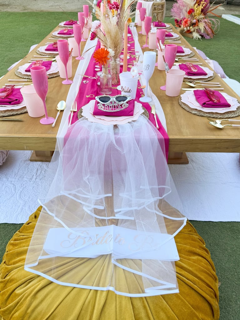 Long decorated table with pink place settings, gold flatware, floral centerpieces, and white tulle runner