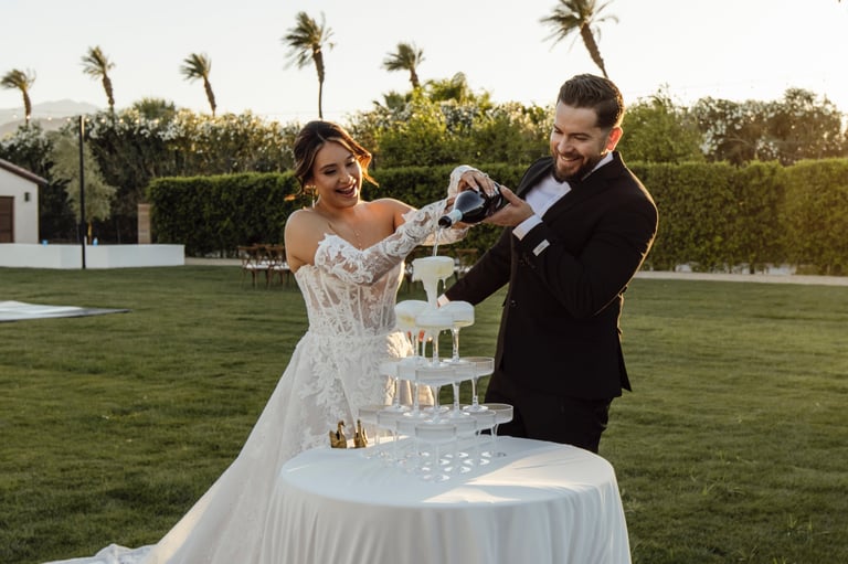Bride and groom pouring sand from bottles during their wedding ceremony in an outdoor garden setting with palm trees.