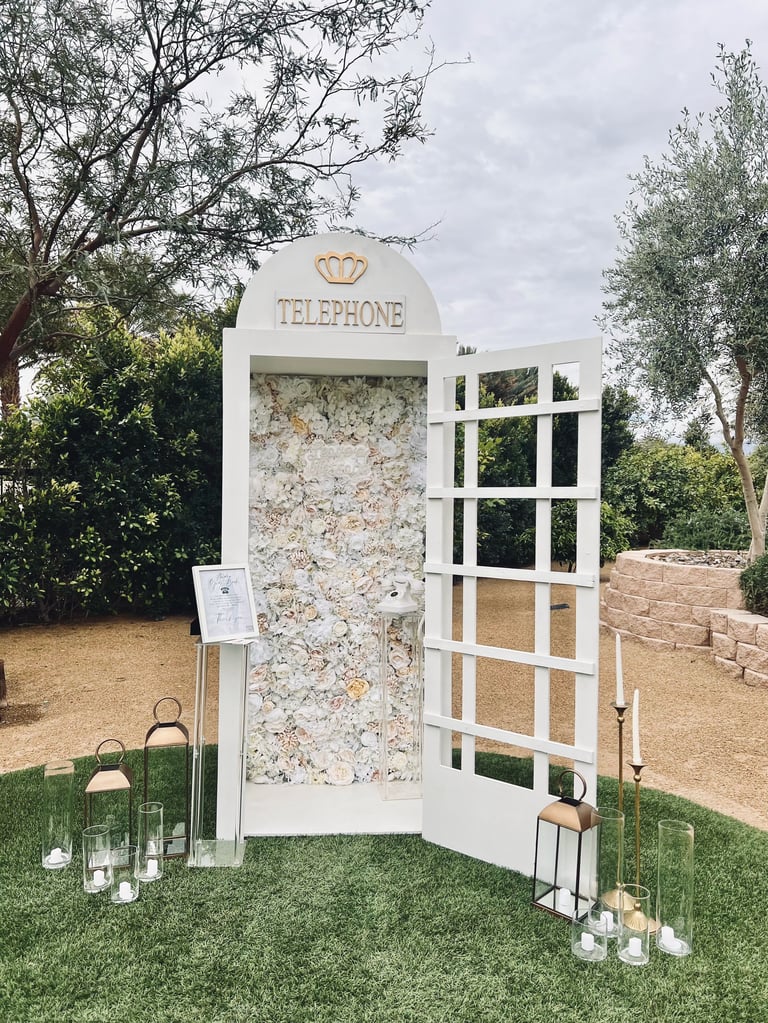 Vintage white British telephone booth with weathered stone back panel, surrounded by trees and decorative candles on grass