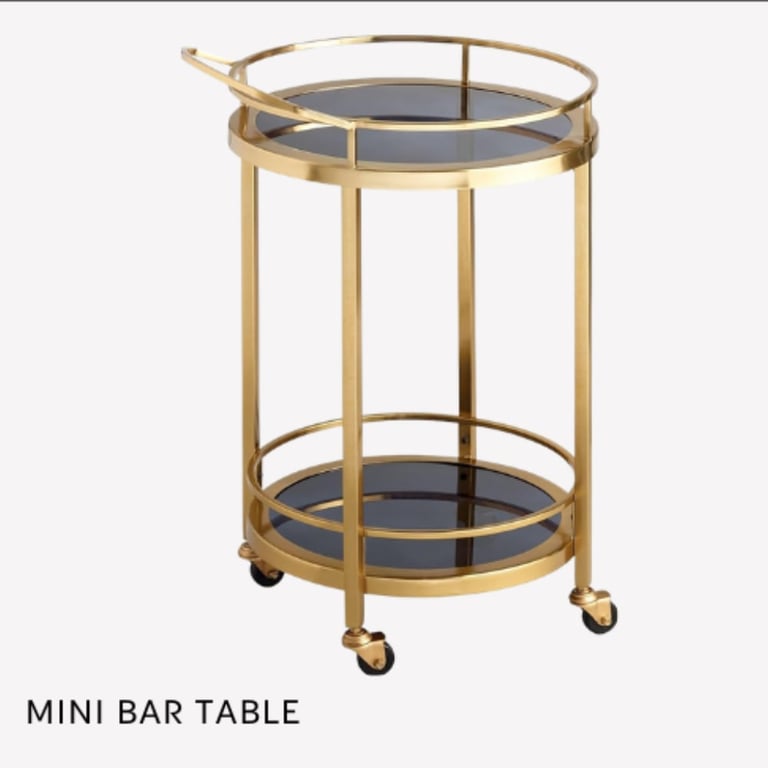 Mini bar table with two black glass shelves, gold metal frame, and casters on wheels