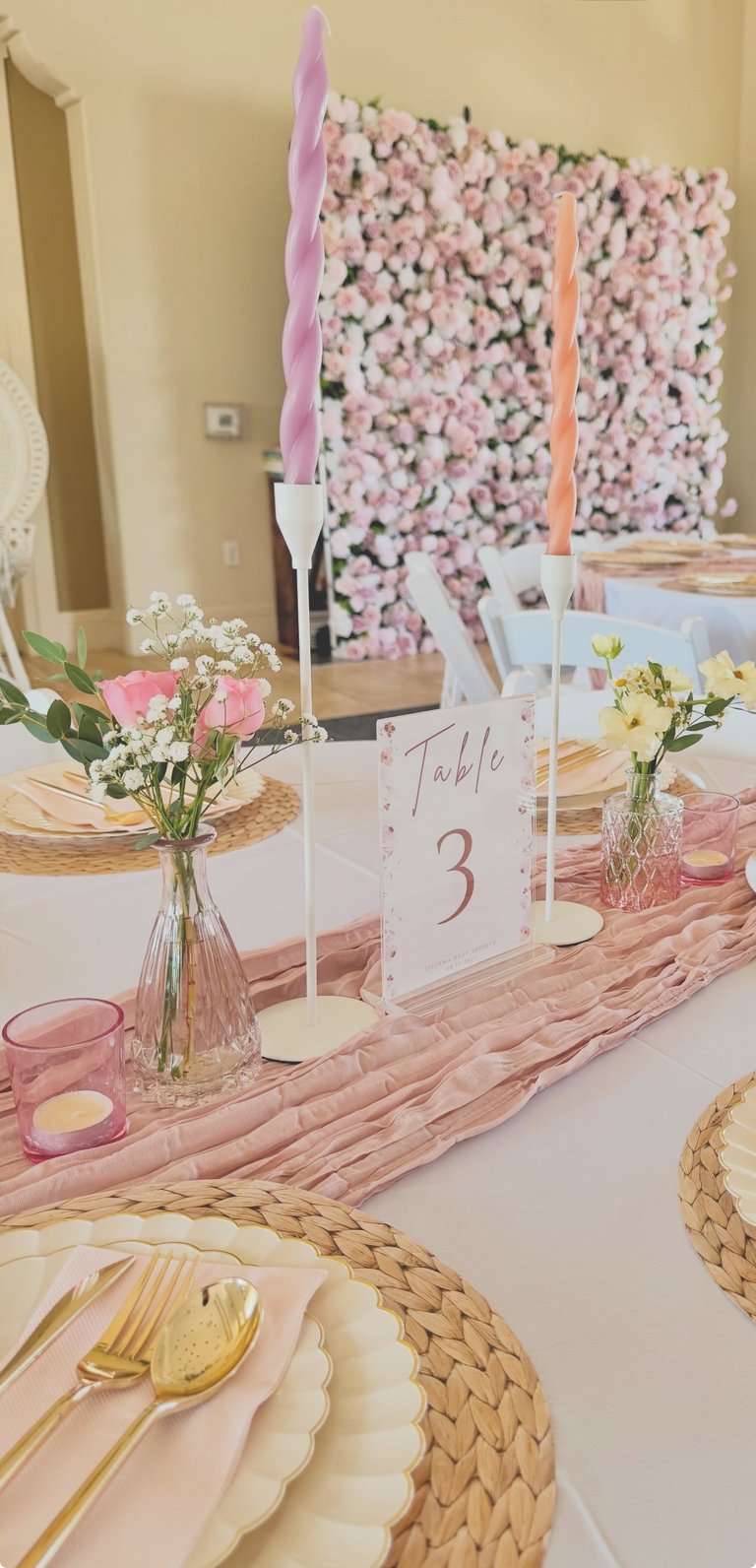 Elegant table setting with pink and white flowers, gold utensils, table number 3, and a pink floral backdrop