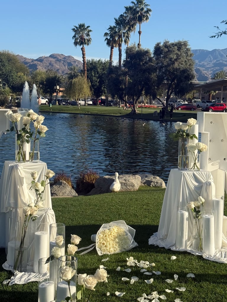 Wedding ceremony setup overlooking a lake with white flowers, palm trees, and mountains in the background