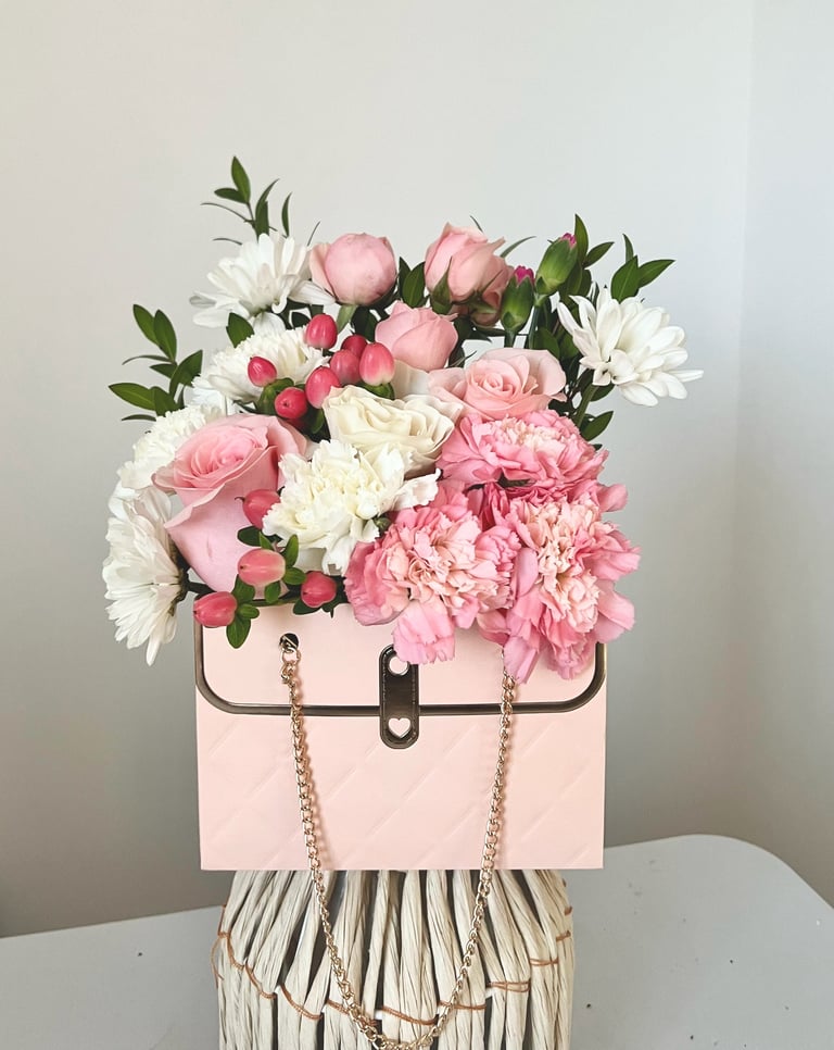 Floral arrangement with pink peonies and white daisies in a pink handbag-shaped vase with chain handles