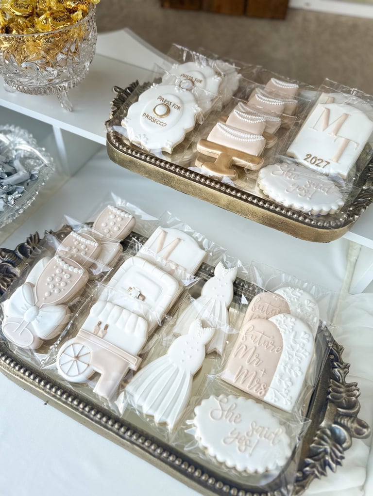Elegant wedding favor display with decorative trays containing personalized towels, soaps, and guest favors in cream and gold tones.