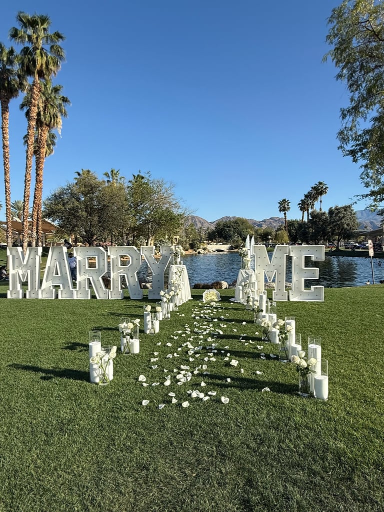 Outdoor proposal setup with large MARRY ME letters by a lake
